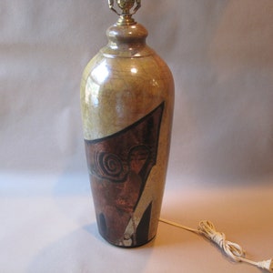 May include: A ceramic table lamp with a brown, gold, and black abstract design. The lamp has a white cord.