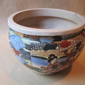 May include: A white ceramic planter with a wide rim and a colorful Japanese-inspired design. The design features flowers, geometric patterns, and a woman in traditional clothing.