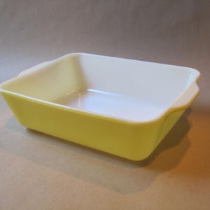 May include: A rectangular baking dish with a bright yellow exterior and a smooth white interior. The dish features integrated handles on two sides and has a deep, open basin design suitable for holding food items during the cooking process.