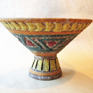 May include: A ceramic bowl with a pedestal base. The bowl is decorated with yellow, orange, green, and red geometric patterns.