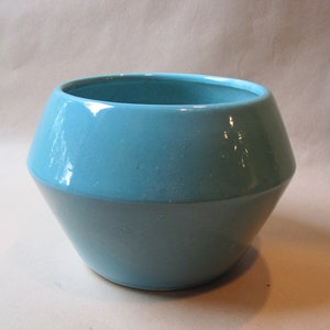 May include: A light blue ceramic planter with a geometric shape. The planter has a smooth, glossy finish.