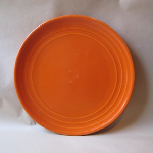 May include: A round, orange plate with concentric rings near the rim. The plate is a solid, vibrant orange color and appears to be made of ceramic or a similar material. The plate is centered in the frame.
