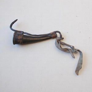 May include: A brown leather hunting horn with a metal hook and a leather strap. The horn is attached to a metal clip with a leather strap.