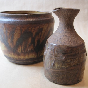 May include: Two ceramic pottery pieces, a brown and yellow glazed bowl and a brown and yellow glazed pitcher with a wide mouth.