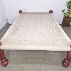 May include: A white woven bed frame with a diamond pattern and red wooden legs. The bed frame is made of natural materials and has a rustic look.
