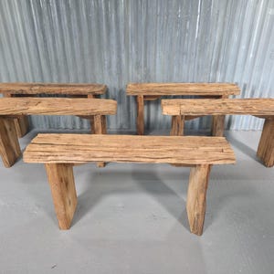 May include: Six rustic wooden benches are displayed. Each bench has a rectangular seat supported by two angled legs. The wood has a natural, weathered appearance with visible grain and texture, in a light brown colour.