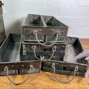 May include: Four vintage metal trays with handles. The trays are stacked on top of each other and are made of a dark grey metal. The trays have a rustic look and would be perfect for displaying plants or other decorative items.