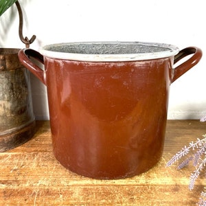 May include: A brown enamel pot with a white rim and two handles. The pot is sitting on a wooden surface.