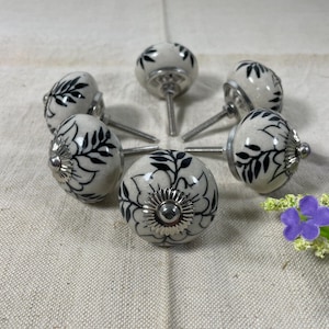 May include: Six white ceramic cabinet knobs with black floral designs and silver metal accents.