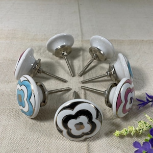 May include: Seven ceramic drawer knobs with floral designs in shades of pink, blue, black, and white. The knobs have silver metal bases and screws.
