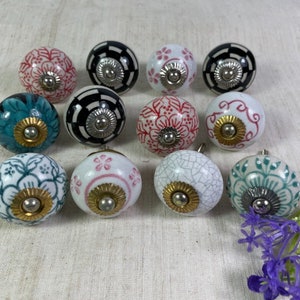 May include: Twelve ceramic knobs with various floral and geometric patterns in shades of white, black, teal, and pink. Each knob has a gold-coloured metal accent.
