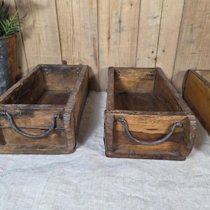 May include: Three rectangular wooden boxes with dark brown wood grain and weathered surfaces. Each box features a curved metal handle attached to the front panel. The boxes are open-topped and have visible metal reinforcement strips along the edges.