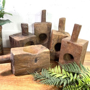 May include: Several weathered wooden blocks with cylindrical handles and circular holes. The blocks are of different sizes and shapes, with a natural, aged appearance. The image also features a floral arrangement and some green foliage.