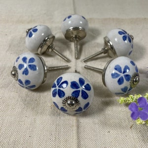 May include: Six white ceramic cabinet knobs with blue floral designs and silver metal bases.