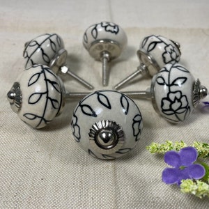 May include: Six white ceramic cabinet knobs with black floral designs and silver metal bases.