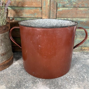 May include: A brown enamelware bucket with two handles. The bucket has a white speckled enamel interior.