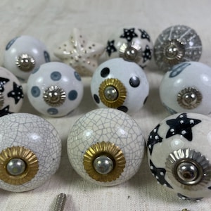 May include: A collection of ceramic knobs with various designs, including stars, polka dots, and cracked glaze. The knobs are white with black and grey accents.