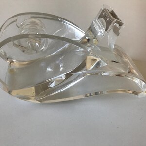 Könnte beinhalten: Ein transparenter Klebebandabroller aus Acryl mit geschwungenem, fließendem Design. Die Struktur verfügt über eine zentrale Spulenhalterung für eine Klebebandrolle und eine gezackte Metallklinge an der Vorderkante zum Abreißen des Klebebands.