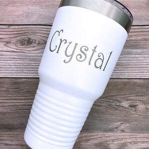 May include: White stainless steel tumbler with a silver lid. The tumbler has a ribbed design and the name "Crystal" is engraved on the front.