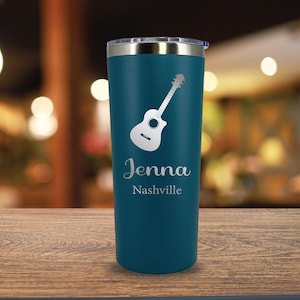 Pode incluir: Um copo de aço inoxidável azul-esverdeado com um gráfico de guitarra prateado e o texto "Jenna Nashville" gravado no lado.
