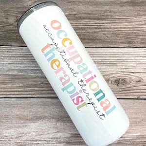 Pode incluir: Um copo de a&ccedil;o inoxid&aacute;vel branco com o texto "occupational therapist" em cores do arco-&iacute;ris.
