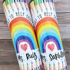 Pode incluir: Dois copos de a&ccedil;o inoxid&aacute;vel com um design de arco-&iacute;ris, cora&ccedil;&atilde;o e l&aacute;pis de cor. O texto "Art to help shape heart" est&aacute; nos copos. Um copo diz "Mrs. Ruiz" e o outro diz "Mrs. Sakhleh".
