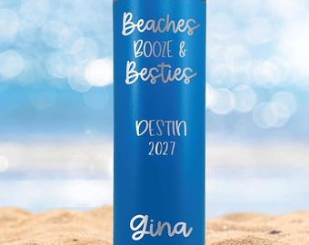 May include: A blue stainless steel tumbler with the text "Beaches Booze & Besties Destin 2027 Gina" in silver lettering.