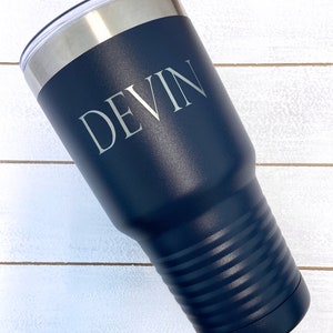 May include: A navy blue stainless steel tumbler with a white lid and the name "DEVIN" engraved on the side.
