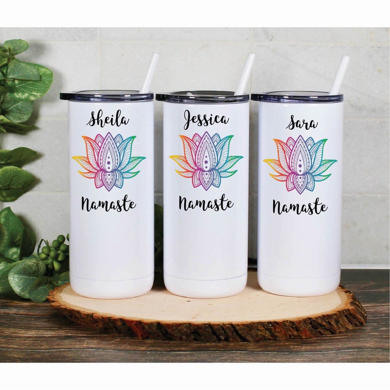 May include: Three white stainless steel tumblers with lids and straws. Each tumbler features a colorful mandala lotus flower design and the words "Namaste" at the bottom. The tumblers are personalized with the names "Sheila", "Jessica", and "Sara".