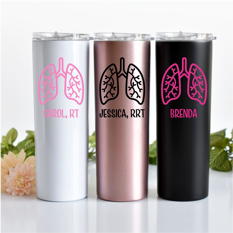 Puede incluir: Tres vasos de acero inoxidable con un dise&ntilde;o de pulm&oacute;n rosa y nombres personalizados. Los vasos son blancos, oro rosa y negros.