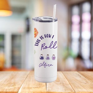 May include: White stainless steel tumbler with a purple design that says "This is how I roll" with three purple potion bottles and the name "Alfira" at the bottom.