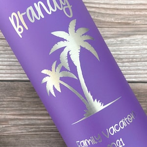 May include: Purple stainless steel water bottle with a silver inscription that reads "Brandy Family Vacation 2021". The bottle features a silver silhouette of two palm trees.