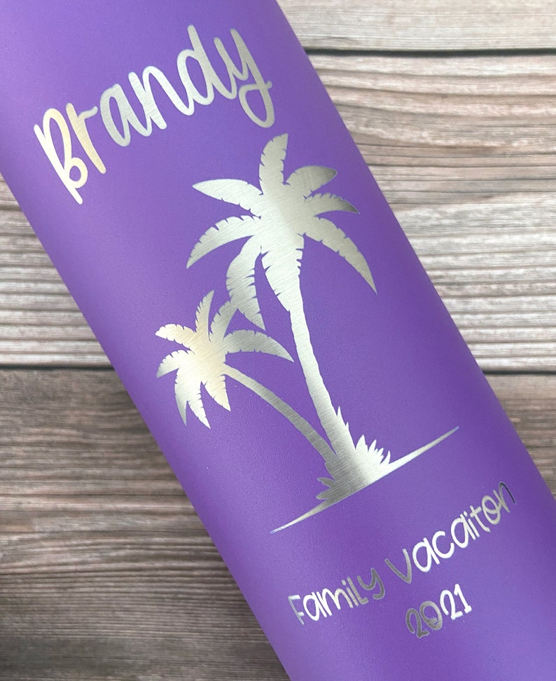 May include: Purple stainless steel water bottle with a silver inscription that reads "Brandy Family Vacation 2021". The bottle features a silver silhouette of two palm trees.