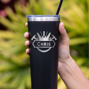 May include: Black stainless steel tumbler with a silver design of tools and the name "CHRIS" engraved on it. The tumbler has a lid and a straw.