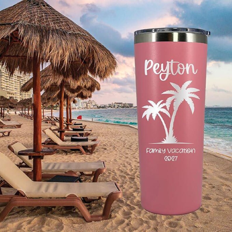 May include: Pink stainless steel travel tumbler with a white palm tree design and the text "Peyton Family Vacation 2027".