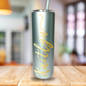 May include: A teal blue stainless steel tumbler with a gold inscription that reads "Raitilyn".