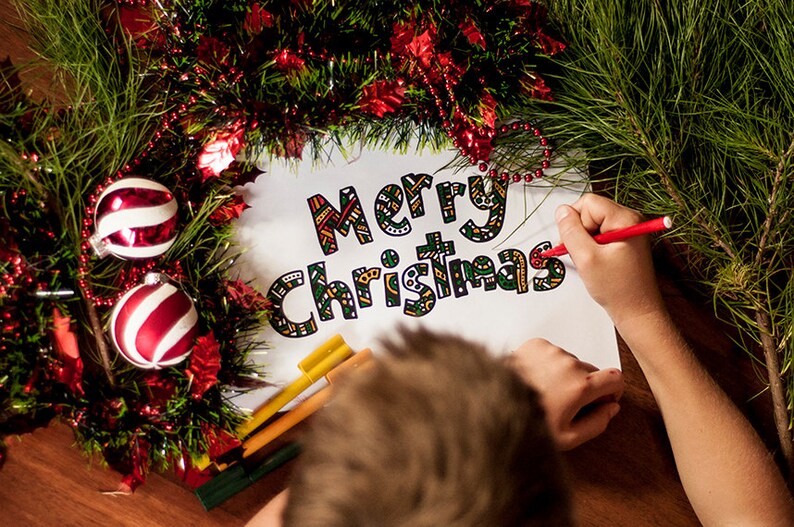 May include: A child colors in a "Merry Christmas" sign with red, green, and yellow markers. The sign is surrounded by a green garland with red and white ornaments.