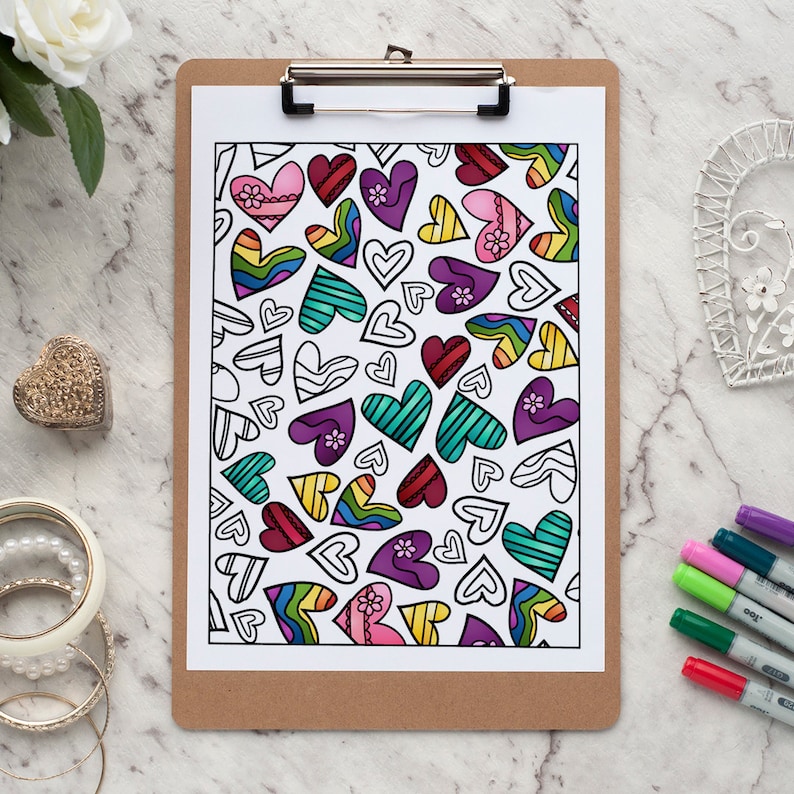 May include: A coloring page with a pattern of hearts in various colors, including red, pink, yellow, green, and purple, is clipped to a wooden clipboard. Some hearts are colored, while others are outlined. Markers are visible.