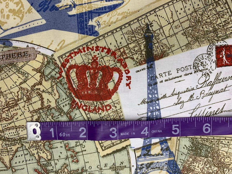 May include: Fabric with a vintage travel theme. The design includes maps, a red crown, the Eiffel Tower, and a postcard. A purple measuring tape shows 60 inches. The fabric has a cream background with blue and brown accents.