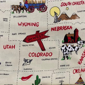May include: Cream-colored fabric with a colorful map of the Western United States. The map includes illustrations of a covered wagon, a cowboy on a horse, and a sign that says "Go West". States like Wyoming, Colorado, and Nebraska are labeled.