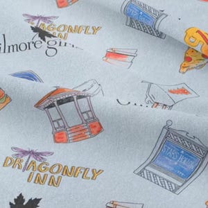 May include: A light blue fabric with a repeating pattern of various illustrations. The illustrations include a dragonfly, a gazebo, a pizza slice, a sign that says "Stars Hollow", and the text "Dragonfly Inn".