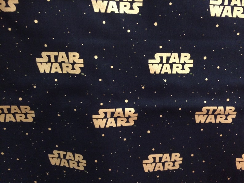 May include: Dark blue fabric with a repeating pattern of the words "STAR WARS" in a gold color. The design includes small, gold-colored dots scattered across the background, resembling stars.