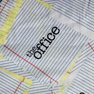 May include: A white fabric with a blue and red grid pattern. The words "the office" are printed in black on the fabric.