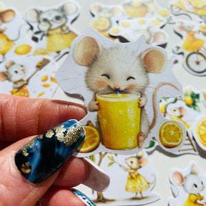 May include: A collection of whimsical stickers featuring cartoon mice enjoying lemons and lemonade. One sticker shows a mouse drinking from a yellow beverage. Other stickers depict mice in yellow dresses and hats, with lemons and bicycles. The stickers have a cheerful, summery theme.