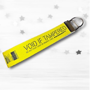 May include: A yellow keychain strap with the text "VOID IF TAMPERED" in black. The strap has a metal ring and a small barcode label. The text "DO NOT PAINT OVER OR REMOVE LABEL" is also printed on the strap.