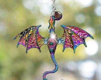 May include: A colorful dragon ornament with iridescent wings and a long, curved tail. The dragon features a jewel-like body with teal and purple accents. It hangs from a silver chain and a black clip.