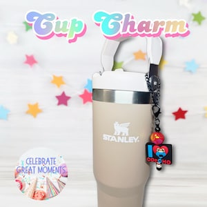 May include: A beige Stanley travel mug with a black handle and a black chain attached to a charm with a red heart and the words "I love Concho" on it. The mug is sitting on a white surface with a string of colorful stars in the background. The text "Cup Charm" is written in pink and blue letters at the top of the image.