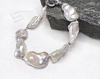 May include: A white baroque pearl bracelet with a silver clasp. The pearls are large and irregular in shape, with a high luster.