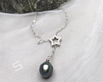 May include: A silver necklace with a star pendant and a black pearl drop. The necklace is on a white fabric background.