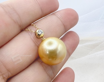 May include: A gold-colored necklace featuring a large, round pearl pendant. The pendant is suspended from a delicate gold chain and accented with a small, sparkling diamond. The pearl has a lustrous, smooth surface.